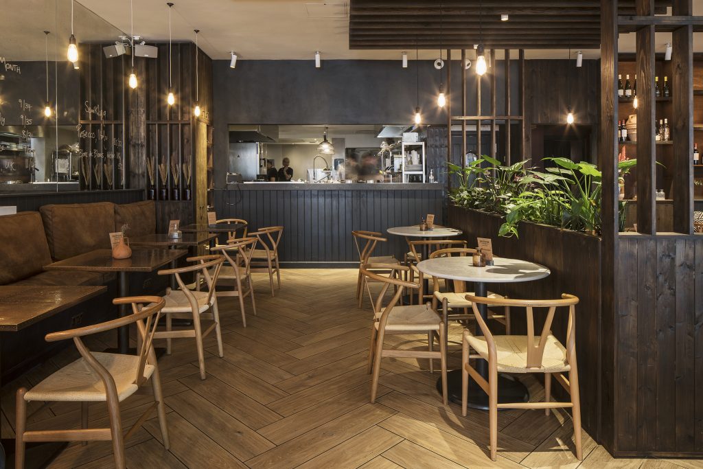 Interior of a cafe with dark wood wall cladding and wishbone chairs. Lost In the Lanes, Brighton. Stickland Wright Interior Design