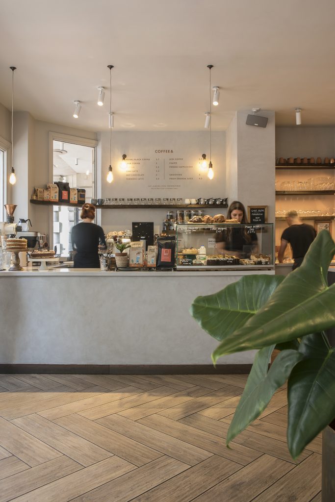 Cafe serving counter design including off-white lime washed bar front. Exposed bulb pendant lights hang above. Stickland Wright Architects and Interior Design, Brighton & Hove